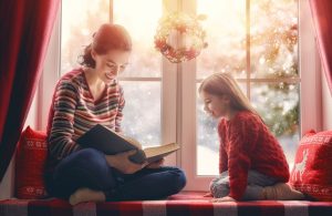 Woman and child seated by a window reading a book