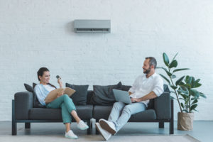 Man and woman seated on couch under ductless wall unit