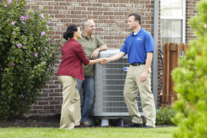 Technician shaking woman's hand with man by central AC unit