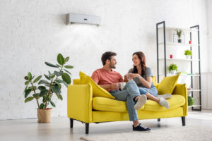 Man and woman seated on yellow couch with wall unit 