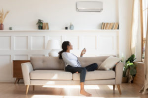 young woman sits on couch using remote control for ductless system