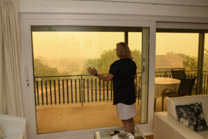 woman stands inside home looking out at smoke from wildfires