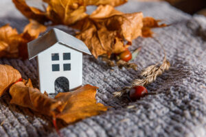 Autumnal Background. Toy house and dried orange fall maple leaves on grey knitted sweater. 